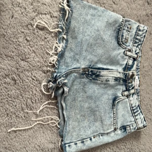 Blå jeansshorts från Denim Day - Säljer ett par snygga blå jeansshorts från Denim Day. De har en fransig kant och klassisk femficksdesign. Perfekta för en avslappnad stil.