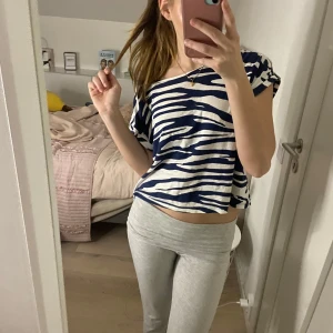 Blå och vit zebramönstrad topp - Säljer en blå och vit zebramönstrad topp med korta ärmar. Toppen har en lös passform och är perfekt för en avslappnad stil. Den är tillverkad i ett mjukt material som känns skönt mot huden.