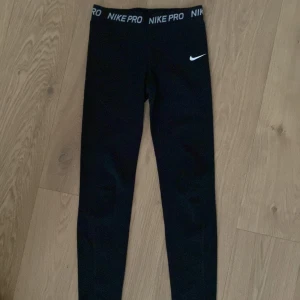 Svarta leggings från Nike Pro - Säljer ett par svarta Nike Pro leggings med elastisk midja och vit logga. Perfekta för träning och bekväma att bära. Midjan har en tydlig Nike Pro-text.