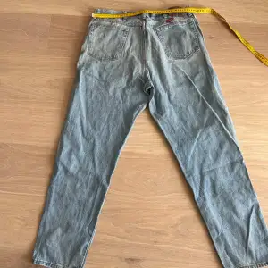 Säljer ett par klassiska blå jeans från Wrangler. De har en rak passform och är tillverkade i slitstarkt denim. Perfekta för en avslappnad stil. Jeansens baksida har två fickor med märkets logga ovanför.