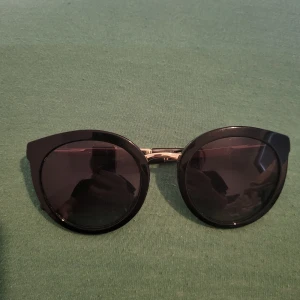 Svarta solglasögon från Dolce & Gabbana - Snygga svarta solglasögon från Dolce & Gabbana med rund form och guldiga detaljer. Perfekta för en stilren look. De har en klassisk design som passar till många olika outfits.