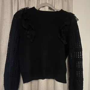 Svart stickad tröja med volangdetaljer - Snygg svart stickad tröja med volangdetaljer på axlarna och hålmönster på ärmarna. Är M men skulle säga mer som S!
