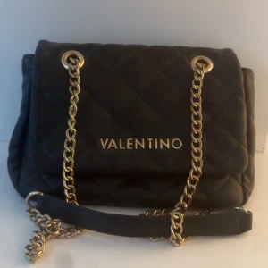 Valentino väska  - Snygg svart quiltad axelväska från Valentino med guldfärgade kedjedetaljer. Det medföljer även orginalpåse till (bild 3). Orginalpris 1545kr kan finnas små små defekter på insidan, inget som är sönder eller märks för tydligt