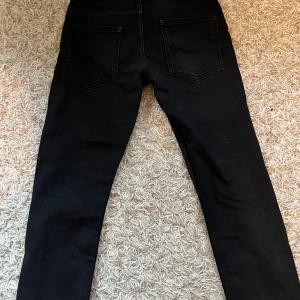 Svarta jeans från Predicted - Snygga svarta jeans från Predicted med klassisk femficksdesign. De har en knappgylf och är perfekta för en stilren look. Passar till många olika outfits och tillfällen.