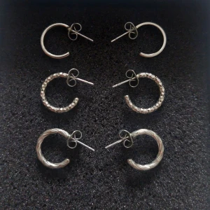 Set med tre par silverörhängen - Säljer ett set med tre par stilrena silverörhängen. Ett par är släta, ett par har en glittrig yta och det sista paret har en vriden design. Perfekta för att mixa och matcha till olika tillfällen.