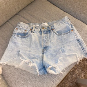 Ljusa jeansshorts från MNG - Säljer ett par ljusa jeansshorts från MNG med fransiga kanter och klassisk femficksdesign. Perfekta för sommardagar och festivaler. De har en knappgylf. De har gått sönder fram ( se bild ) på båda sidorna men de är inget man störs av. Storlek 36, 50 kronor plus frakt