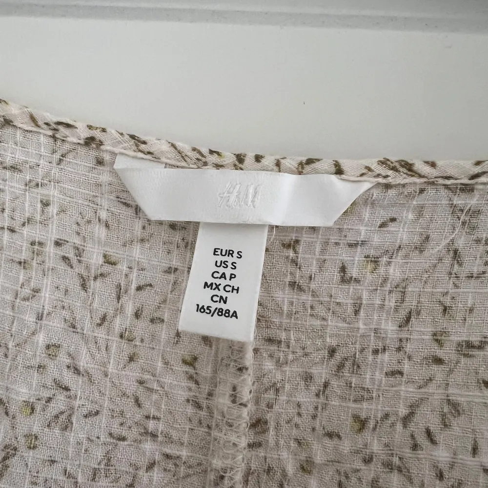 Charmig beige klänning från H&M med ett subtilt blommönster. Klänningen har en v-ringad design och puffiga trekvartsärmar som ger en romantisk touch. Perfekt för vårens och sommarens tillfällen.. Mekot.