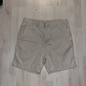 Linne shorts - Snygga beige shorts med elastisk midja och snörning för extra komfort. Perfekta för varma dagar med sin lätta och luftiga design. De har praktiska sidofickor och en bakficka för förvaring.