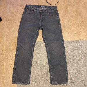 Grå/Blå jeans från Dressmann - Säljer ett par klassiska blå jeans från Dressmann i relaxed fit. De har en traditionell femficksdesign och knappar i bronsfärg. Perfekta för en avslappnad stil.Har haft på de 1-2gånger