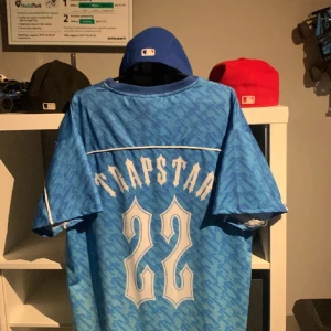 Blå t-shirt från Trapstar - Säljer en blå t-shirt från Trapstar med ett coolt kamouflagemönster. Tröjan har korta ärmar och ett stort tryck med siffran 22 på baksidan. Perfekt för en avslappnad stil.