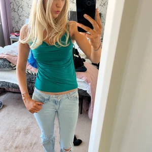 Turkos linnetopp - Säljer en snygg turkos linnetopp med smala axelband och en draperad halsringning. Perfekt för sommardagar eller en kväll ute. Toppen är figurnära och ger en stilren look.