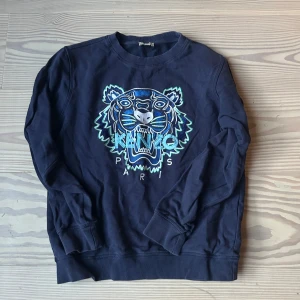Kenzo tröja - Säljer en snygg mörkblå sweatshirt från Kenzo med ett coolt tigerbroderi i blått och grönt på framsidan. Tröjan har långa ärmar och ribbade muddar vid ärmslut och nederkant. Perfekt för en stilren look!