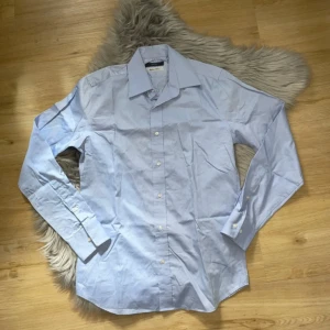 Ljusblå skjorta från Riley - Snygg ljusblå skjorta från Riley med klassisk krage och knappar framtill. Tillverkad i 100% bomull för en skön och luftig känsla. Perfekt för både formella och avslappnade tillfällen.