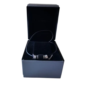 Svart och silver halsband från Emporio Armani - Elegant halsband från Emporio Armani med en kombination av svart läderrem och silverkedja i stål!! Smycket har en unik design med flera ringar i silver och svart i mitten. Perfekt för att ge en stilren touch till din outfit.