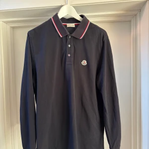 Marinblå långärmad pikétröja från Moncler - Säljer en stilren marinblå långärmad pikétröja från Moncler. Det är storlek XL men sitter som en L/M
