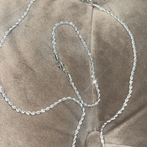 Silverfärgat halsband och armband - Snyggt set med ett silver halsband och matchande armband i tvinnad design. Perfekt för att ge en stilren touch till din outfit. Halsbandet har en praktisk karbinhake för enkel användning.☀️😍