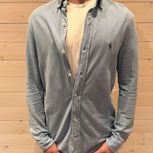Ljusblå skjorta från Ralph Lauren - Snygg ljusblå skjorta från Ralph Lauren med klassisk krage och knappar framtill. Skjortan har en broderad logotyp på bröstet och långa ärmar. Perfekt för en stilren look.