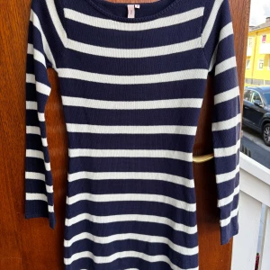 Randig stickad klänning från Nelly - Mysig stickad klänning från Nelly i marinblått och vitt med horisontella ränder. Modellen är kroppsnära med trekvartsärm och rund halsringning. Perfekt för dig som gillar en klassisk och stilren look.