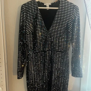 Glittrig svart klänning från NLY One - Supersnygg svart klänning från NLY One med glittriga paljetter i ränder över hela klänningen. Djup v-ringning framtill och långa ärmar. Perfekt för dig som vill sticka ut med en festlig look! Aldrig använd. Nassar mig som vanligt har XS. Men passar också dem med större storlekar såklart.