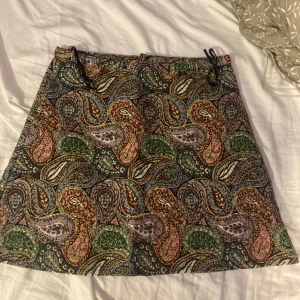 Mönstrad kortkjol från Zara - Färgglad kortkjol från Zara med paisleyinspirerat mönster i grönt, blått, lila och brunt. Kjolen har en lätt A-linjeform och dragkedja i sidan. Perfekt för dig som gillar unika prints och vill sticka ut lite extra.