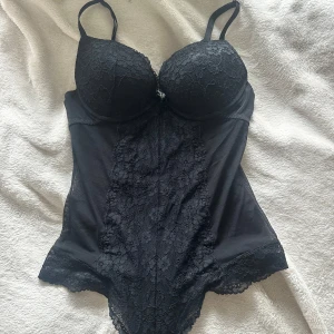 H&m body - Supersnygg svart body med vadderade kupor och bygel, täckt av blommig spets framtill och mesh på sidorna. Justerbara axelband och fina spetsdetaljer längs kanterna. Perfekt för att lyfta din outfit med en edgy vibe. Kuporna passar cs 70/75B och 70C 