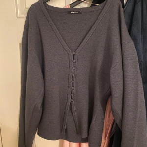 Mörkgrå kofta från Gina Tricot - Mysig mörkgrå kofta från Gina Tricot med v-ringning och dekorativa knappar framtill. Långärmad och i mjukt stickat material, perfekt för lager-på-lager. Enkel och stilren design som passar till allt.