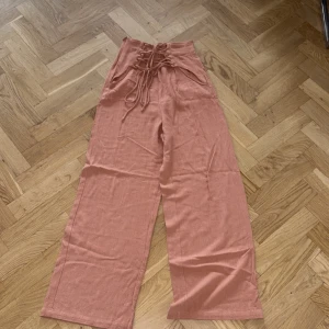 Rostfärgade linnebyxor från Shein - Snygga rostfärgade linnebyxor från Shein med hög midja och breda ben. Byxorna har cool snörning framtill och dragkedja i sidan. Perfekta för dig som gillar en relaxed och trendig stil.