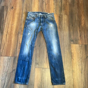 Blå jeans från Diesel - Snygga blå jeans från Diesel med klassisk femficksdesign och slitna detaljer. Jeansen har raka ben och tydliga kontrastsömmar. Perfekta för dig som gillar en avslappnad och tidlös look. Billiga på grund av att den har blivit ett lite hål på dem 