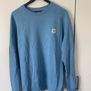 Blå loose fit tröja från Lee - Säljer en ljusblå sweatshirt från Lee i loose fit-modell. Tröjan har rund halsringning, ribbade muddar och en liten Lee-logga på bröstet. Tillverkad i mjuk bomull, perfekt för chill dagar eller när du vill ha en avslappnad stil.
