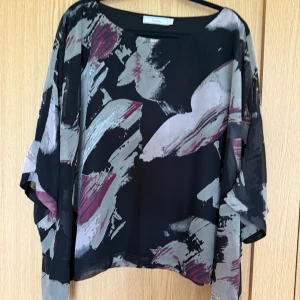 Svart blus med abstrakt mönster Fransa - Säljer en luftig svart blus från Fransa med stora abstrakta penseldrag i grått och vinrött. Blusen har vida, trekvartsärmar och är tillverkad i ett tunt, transparent material som ger en cool och flowy känsla. Perfekt för dig som gillar statement-plagg med konstnärlig vibe. Med blusen tillhör ett underlinne. 