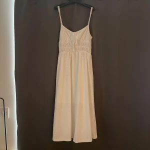 Vit sommarklänning med knyt - Superfin vit klänning med smala axelband, broderade hål och knyt framtill. Klänningen har v-ringning, resår i midjan och är tillverkad i ett lätt bomullstyg. Perfekt för varma dagar och har en luftig, avslappnad passform. Man kan justera axelbanden. Jag har storlek xs och säljer denna för att den är lite för stor och sitter lite hängigt på mig.