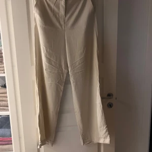 Beiga vida byxor från Pieces L - Snygga beiga byxor från Pieces i modellen PCChrista Pants. De har en rak och vid passform, resår i midjan baktill och bälteshällor. Materialet är mjukt , perfekta för en chill och stilren look.