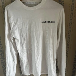 Vit långärmad tröja Calvin Klein Jeans - Vit långärmad tröja från Calvin Klein Jeans. Tröjan har svart logga tryckt på bröstet och längs ena ärmen. Enkel och clean design med rund halsringning, perfekt för en stilren look.