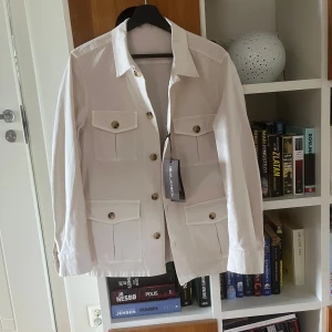 Beige overshirt från oscar Jacobsson - Snygg beige overshirt från Oscar Jacobson med fyra stora fickor framtill och klassisk krage. Modellen heter Safari shirt jacket och är helt ny och endast testad men gick inte att lämna tillbaka. Nypriset är 2499