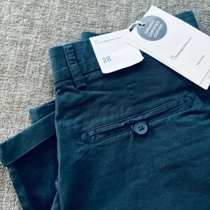 Helt nya  shorts från Knowledge Cotton strl 28 - Helt nya superfina marinblå Knowledge Cotton Apparel chinos shorts i ekologisk bomull. Rak passform med bälteshällor, sidfickor och bakficka med knapp.  Storlek 28. Nypris 699 kr. 