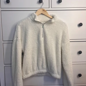 Vit fluffig fleece-tröja half zip - Supermjuk och fluffig vit fleece-tröja med halv dragkedja och hög krage. Perfekt för kyliga dagar när du vill vara både varm och snygg. Långärmad och med relaxed fit som ger en chill vibe.