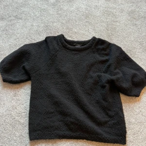 Svart stickad tröja från Lindex XS - Mysig svart stickad tröja från Lindex i storlek XS. Tröjan har en rund halsringning och korta ärmar. Den har en lite bubblig textur. 