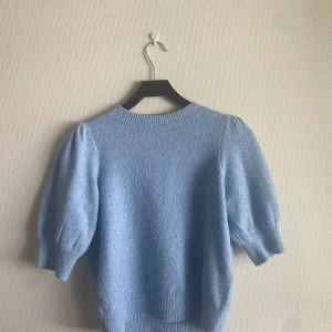 Ljusblå stickad tröja -  jusblå stickad tröja med puffärmar och ribbade muddar. Tröjan har en rund halsringning.