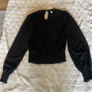 Svart blus från New Yorker - Supersnygg svart blus från FB Sister i storlek XS. Blusen har långärmade puffärmar, smockad midja och är dekorerad med små prickar i tyget för en cool struktur. Rund halsringning med knapp i nacken💗