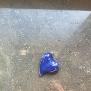 Blått hjärthänge i keramik - Unikt handgjort hjärthänge i blå och vit keramik. Framsidan är glansig och djupblå med fina nyanser, medan baksidan är matt och ljus. Perfekt som smyckesdetalj eller personlig accessoar.