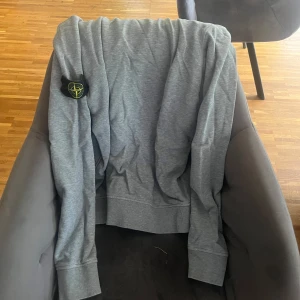 Grå Stone Island sweatshirt - Säljer en grå sweatshirt från Stone Island med den klassiska loggan på vänster ärm. Tröjan har rund hals, långa ärmar och är tillverkad i mjuk bomull. Perfekt för en chill och stilren look.