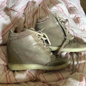 Beige Isabel Marant liknande sneakers med klack   - Snygga beige sneakers från Esprit med kilklack, snörning och dragkedja på sidan. Skorna är i skinn och mocka med detaljer i textil runt ankeln. Perfekta för dig som vill ha lite extra höjd men ändå en sportig look.