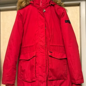 Röd parkasjacka med fuskpäls från Navahoo - Helt ny, tyvärr kom den inte till användning då dottern påtalar detsamma i år. Röd parkasjacka från Navahoo med stor huva och fuskpäls, perfekta stora fickor och ribbade muddar vid ärmsluten. Jackan har dragkedja och knappar framtill, samt en klassisk parkaslook som håller dig varm under kalla dagar.