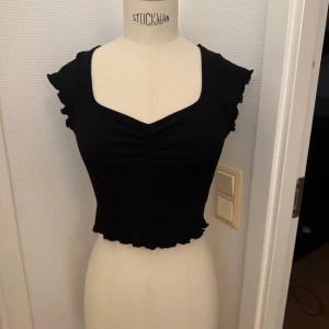 Svart topp XS - XS Snygg svart  topp med volangärmar och rynkdetalj framtill. Nyskick! Toppen har en djup v-ringning och ribbad struktur i tyget. Hämtas på Hägerstensåsen eller skickas. 