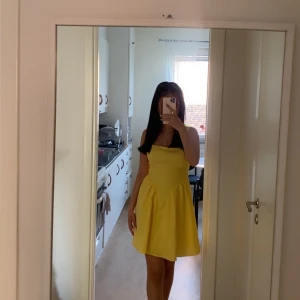 Gul kort klänning med axelband - Säljer en söt gul kort klänning med smala axelband och utställd kjol. Klänningen har en enkel och fräsch design som ger sommarkänsla. Perfekt för dig som vill sticka ut med färg och stil.