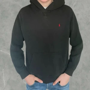 Svart hoodie från Ralph Lauren - Klassisk svart hoodie från Polo Ralph Lauren med liten röd logga broderad på bröstet. Det är storlek (18-20) vilket motsvarar ungefär S i herr storlek. Den är i fint skick utan några defekter eller likande. Vid frågor eller funderingar är de bara att höra av sig.