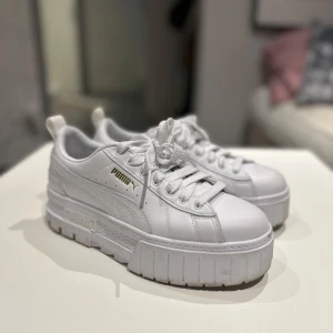 Vita chunky sneakers från Puma - Säljer ett par vita chunky sneakers från Puma med plattformssula och gulddetaljer. Skorna har snörning, rund tå och är tillverkade i skinn. Perfekta för dig som gillar en sportig och trendig look med extra höjd.
