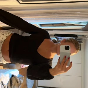 Svart långärmad topp Gina Tricot XS - Svart långärmad topp från Gina Tricot i storlek XS. Toppen har v-ringning framtill, croppad passform och en snygg öppen rygg med knytband upptill. Perfekt för dig som gillar trendiga detaljer och stilren look.