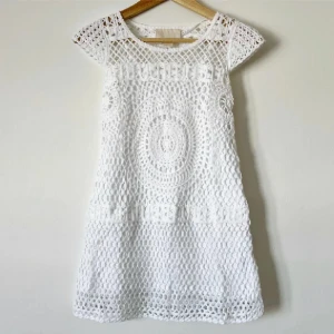 Vit virkad kortklänning i bomull - Superfin vit kortklänning i virkad bomull med snyggt cirkelmönster och korta ärmar. Perfekt för sommarens alla tillfällen, med luftig känsla och unik struktur. Snygg att styla med sandaler eller sneakers för en chill look.