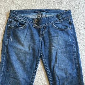 Blå bootcut jeans med broderad detalj - Snygga blå jeans från Denim Bershka med bootcut passform och slitna detaljer. Byxorna har tre knappar i gylfen och klassiska bakfickor.